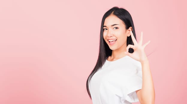 Portrait Asian beautiful young woman standing, She made finger OK symbol sign to agree side away looking at camera, studio shot isolated on pink background, Thai female agree hand sign copy space