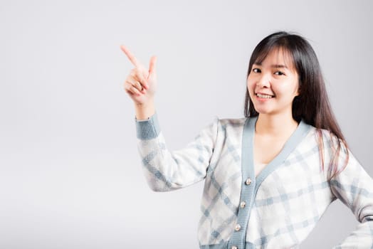 Smiling happy woman pointing finger out space, Portrait Asian beautiful young female point into empty looking to side away, studio shot isolated on white background with copy space