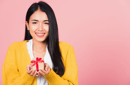 Portrait of happy beautiful Asian young woman smiling holding small gift box on hands, studio shot isolated on pink background, Birthday, New year, Christmas, valentine, holiday day concept