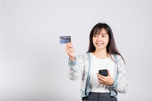 Woman excited smiling hold mobile phone and plastic debit credit bank card for payment studio shot isolated white background, happy young female using smartphone buy and pay online shopping