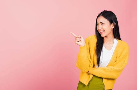 Asian happy portrait beautiful cute young woman standing pointing finger side away presenting product looking to away side, studio shot isolated on pink background with copy space