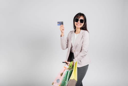 Woman with glasses shopper smile hold online shopping bags, smartphone and credit card for payment, Portrait excited happy Asian female sale mobile financial application isolated on white background