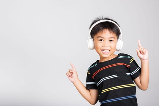 Little cute kid boy 5-6 years old listen music in wireless headphones in studio shot isolated on white background, happy Asian children smiling listening audio and dancing, entertainment lifestyle