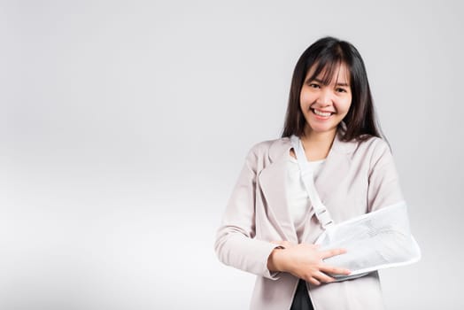 Arm broken. Business woman confident smiling broken arm after accident and wear arm splint for treatment, excited happy Asian female sling support hand studio isolated on white background, copy space
