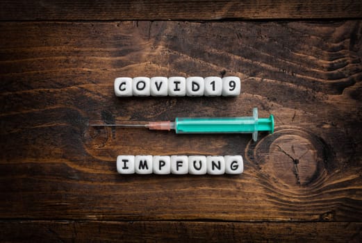 Corona virus Covid-19 vaccine text in German on wooden background