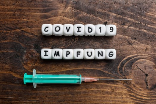 Corona virus Covid-19 vaccine text in German on wooden background