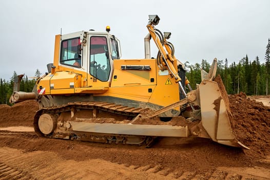 A yellow tractor levels the site with sand. High quality photo