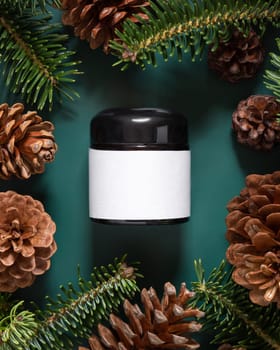 Brown glass jar near fir branches and pine cones on dark green top view. Brand packaging mockup. Skincare beauty product, cream or serum. Healthcare natural cosmetics concept