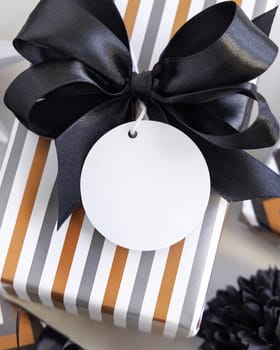 Present with round blank gift tag and black bow close up. Gift boxes wrapped in Striped geometric paper near black and white decor. Christmas, New Year, Birthday, Anniversary label mockup