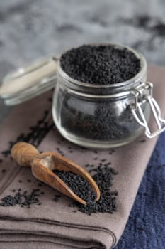 Indian spice Black cumin (nigella sativa or kalonji) seeds glass jar with a wooden scoop, close up. Traditional asian medicine, healthy and vegetarian food concept