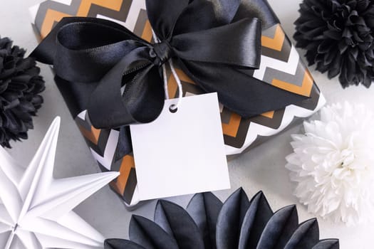 Present with blank square gift tag and black bow close up. Gift boxes wrapped in Striped and chevron geometric paper near black and white decor. Christmas, New Year, Birthday, Anniversary label mockup
