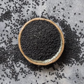 Indian spice Black cumin (nigella sativa or kalonji) seeds in bowl on grey table top view. Traditional medicine, healthy and vegetarian food concept.