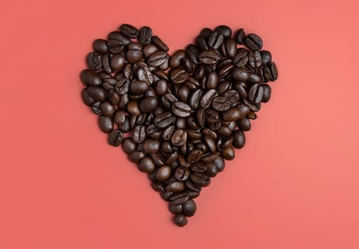 Heart made of Roasted Coffee beans top view on pink background. Represent breakfast, love, energy, freshness or aroma