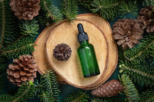 Green Pipette Dropper Bottle between fir branches and pine cones on wooden piece top view. Brand packaging mockup. Dark cream container for skincare product, cream or serum. Healthcare concept. Natural cosmetics.