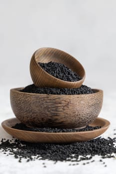 Indian spice Black cumin (nigella sativa or kalonji) seeds in wooden bowls on white table close up. Traditional medicine, healthy and vegetarian food concept.