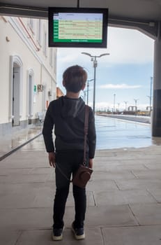 Child boy at railway station looking to departure monitor. Travel on train with children concept