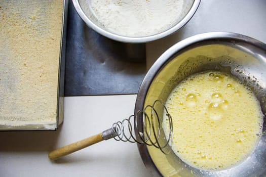 Whipped egg in a silver bowl, flour and baking tin
