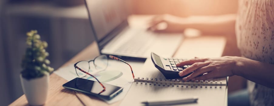 Woman working with laptop and calculator at home office. Panoramic view. Concept of the freelancer.