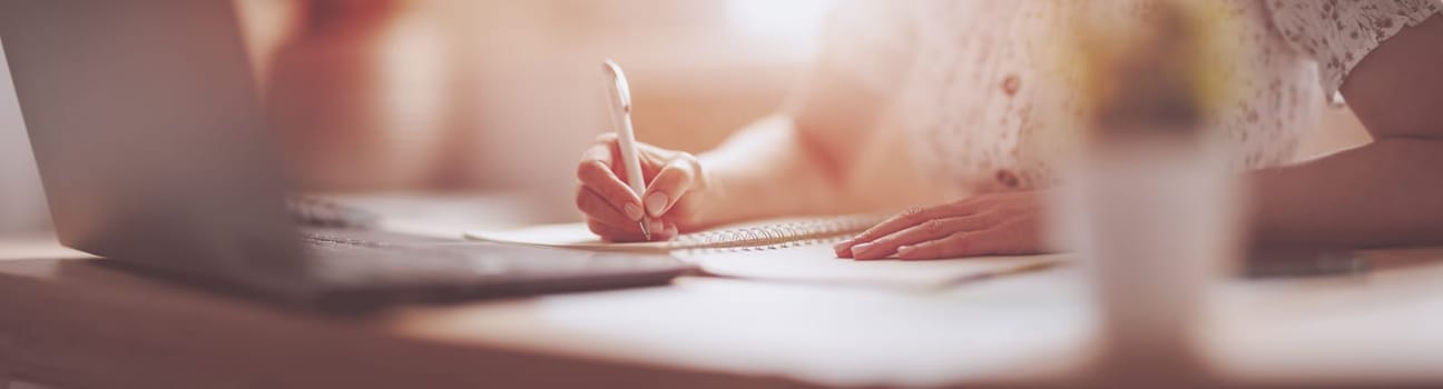 Woman writing in notebook at the office. Close-up panoramic view. Concept of the freelancer and of doing business at home.