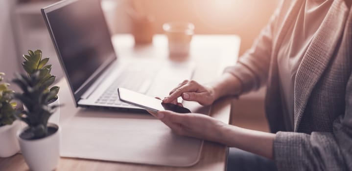 Woman with smartphone in her hand working on the laptop in office. Place of work.