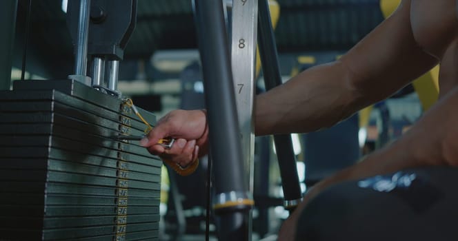 Closeup hands of athlete man chooses weight in the sports equipment in exercise machine, muscle sportsman choosing different weightlifting options for lifting training workout at fitness gym
