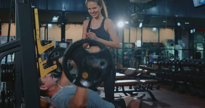 Personal trainer helping muscle man bench press weightlifting with barbell flexing muscles, woman training the man exercising power gymnastics, Sport fit workout bodybuilding concept