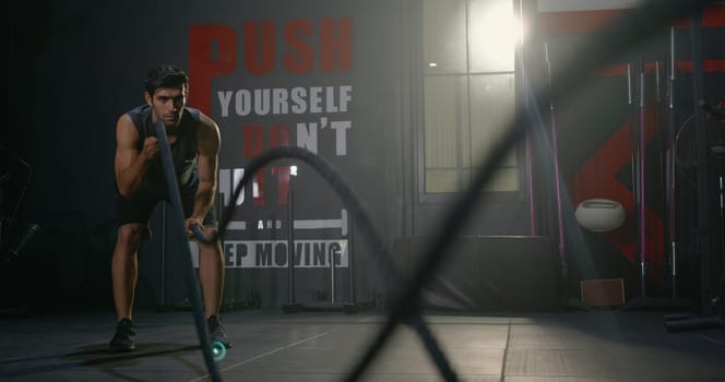 Muscular athletic Caucasian young man strong effort with battle rope waves doing exercise while working out in fitness gym, Cross fit training, People power sport health lifestyle concept