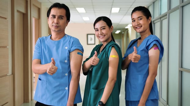 Medical personnel showing thumbs up and bandage with plaster on arm after getting Covid-19 vaccine, happy nurse woman and man standing at hospital, Covid-19 vaccination concept
