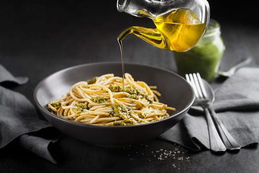 Served spaghetti with fresh basil pesto and pouring with olive oil bottle closeup
