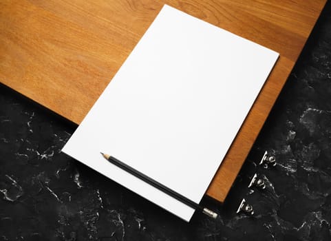 Blank white letterhead, pencil and metal clips. Blank branding template on wooden board background.