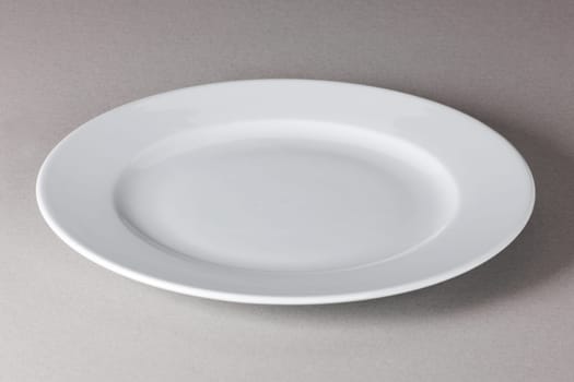 A raised view of a white dinner plate on neutral background with shadow