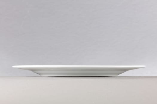 A side view of a white dinner plate on neutral background