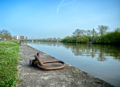 rusty metal loops for anchoring boats on the riverside at daytime, river and bridge in the background