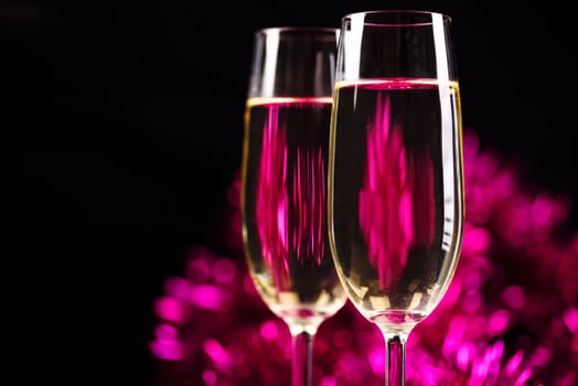 Two champagne glasses in front of purple sparkling background