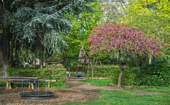 Idyllic playground with play equipment surrounded by various trees, blooming tree, swing and rotation equipment for children
