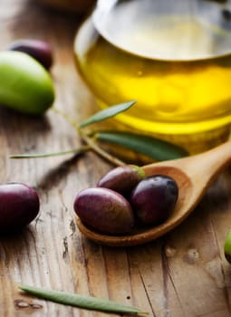 Olives in wooden spoon and olive oil on rustic table