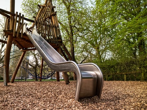 Playground with fokus on a silvery slide, wooden climbing frame in the background, worms-eye view