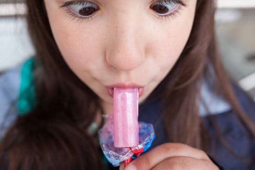 Little girl licking a whistle or melody pop. She is making a funny face