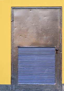 close up of a metal door of a transformer building, yellow painted walls, blue painted ventilation slits