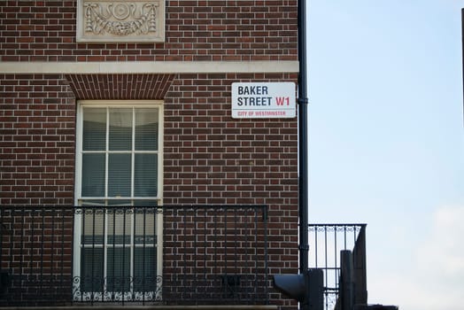 Baker Street sign affixed on dark brick wall next to empty window to one side and balcony to the other. Lots of copy space.