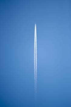 Aircraft flying high above leaving well-defined condensation trail behind it. Isolated against blue sky.