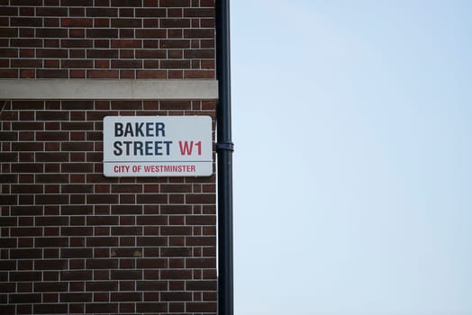 Baker Street sign affixed on dark brick wall next to drainage pipe. Lots of copy space.