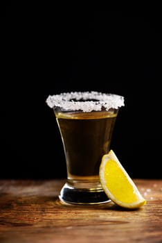Tequila shot with salt on wooden table.