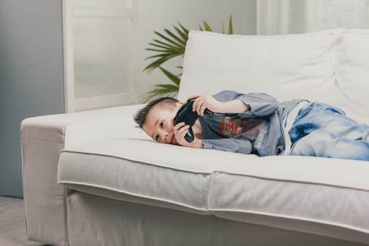 Young boy lying on a sofa playing video games as he spends a lazy day at home over the weekend or summer vacation