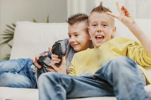 Happy young boy giving Victory sign with his fingers after beating his brother at a video game as they relax together on a sofa at home
