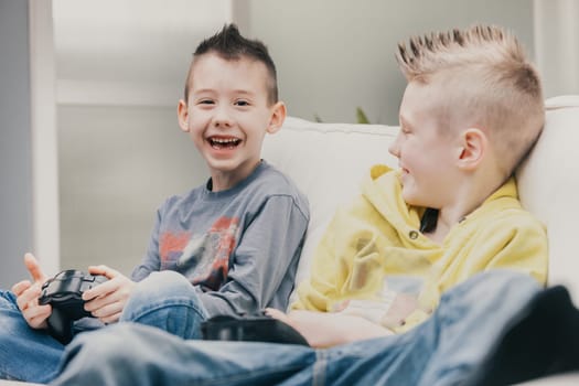 Vivacious playful little boy enjoying a good laugh as he looks at the camera while playing video games on a sofa at home with his brother in a candid portrait