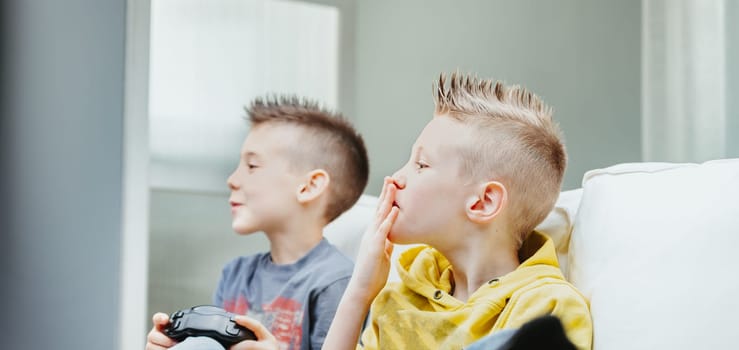 Young brothers playing video games watching in trepidation pursing their lips in anticipation in a close up side portrait indoors at home