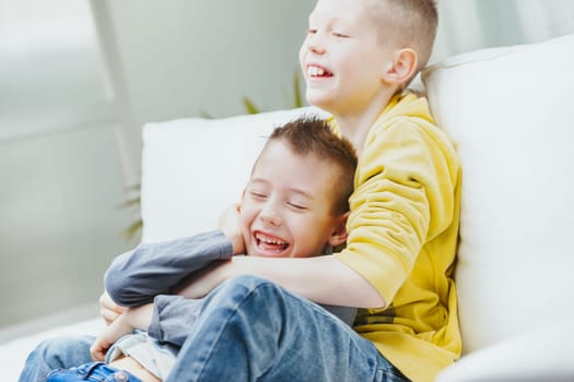 Two happy young brothers romping on a sofa together laughing and cuddling in a close up family portrait