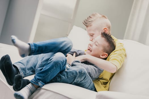 Two laughing little boys playing on a sofa at home cuddling as they tickle each other enjoying spending quality family time together