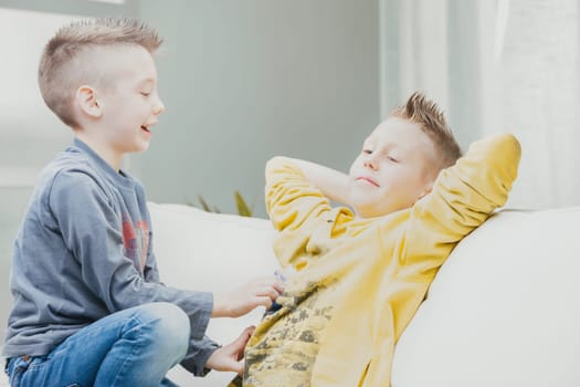 Mischievous young boy tickling his older brother on the stomach as they relax together on a sofa in a high key image